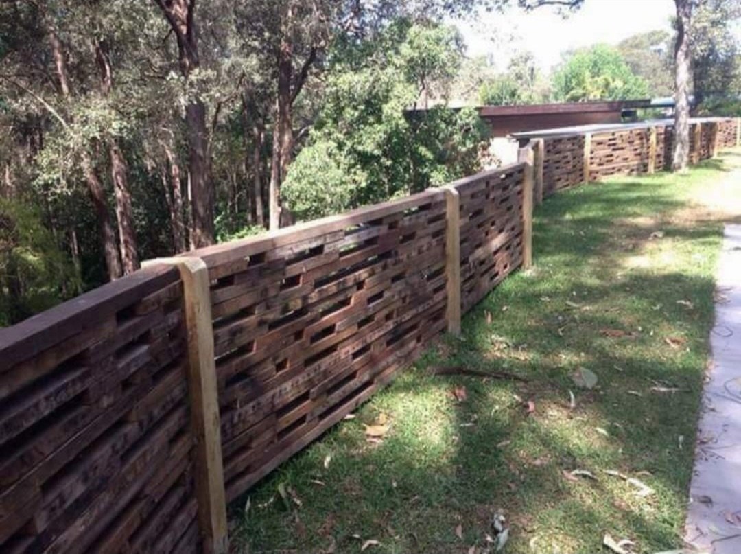 A dark woven timber feature fence running through an established Shoalhaven garden