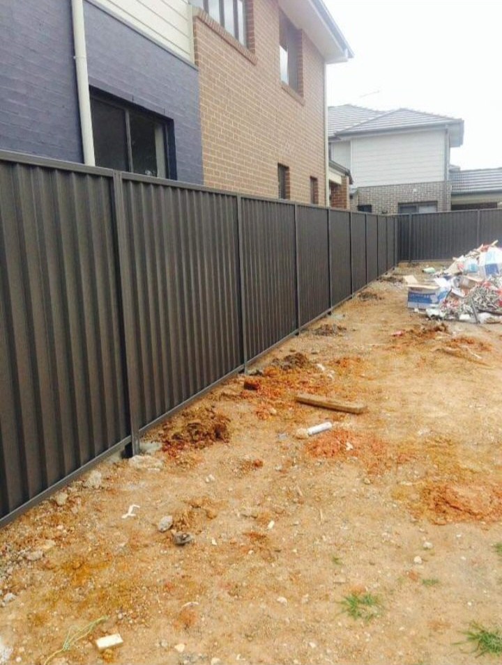 A dark Colorbond fence run along a new build