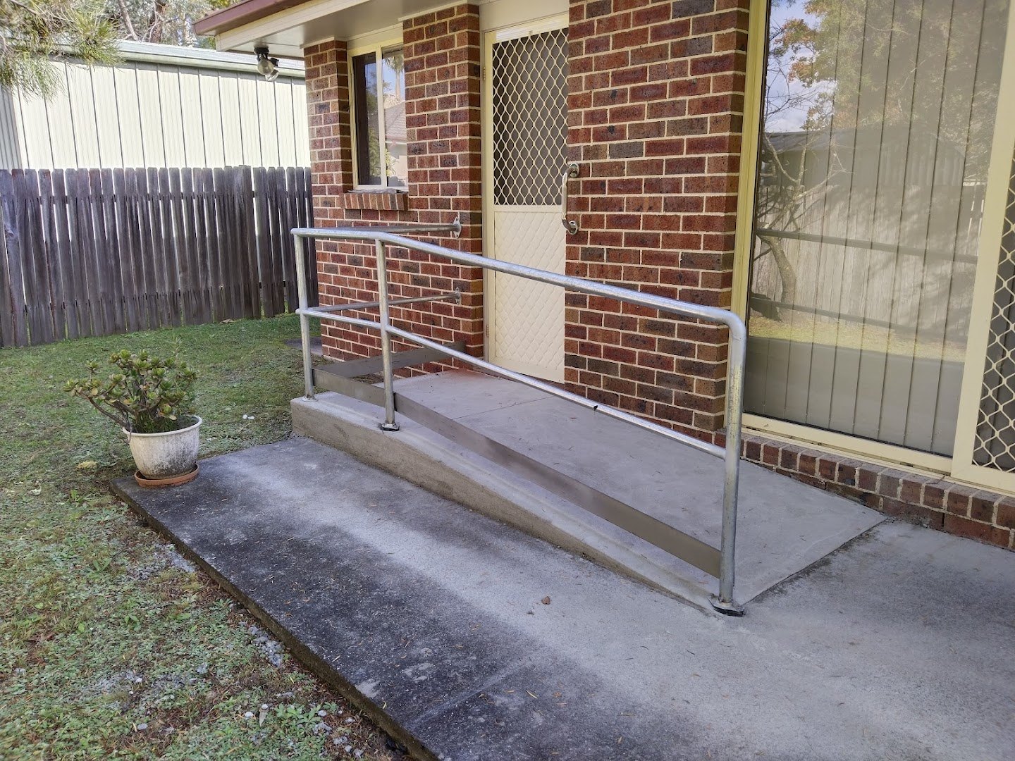 A concrete ramp and handrail at a brick entry